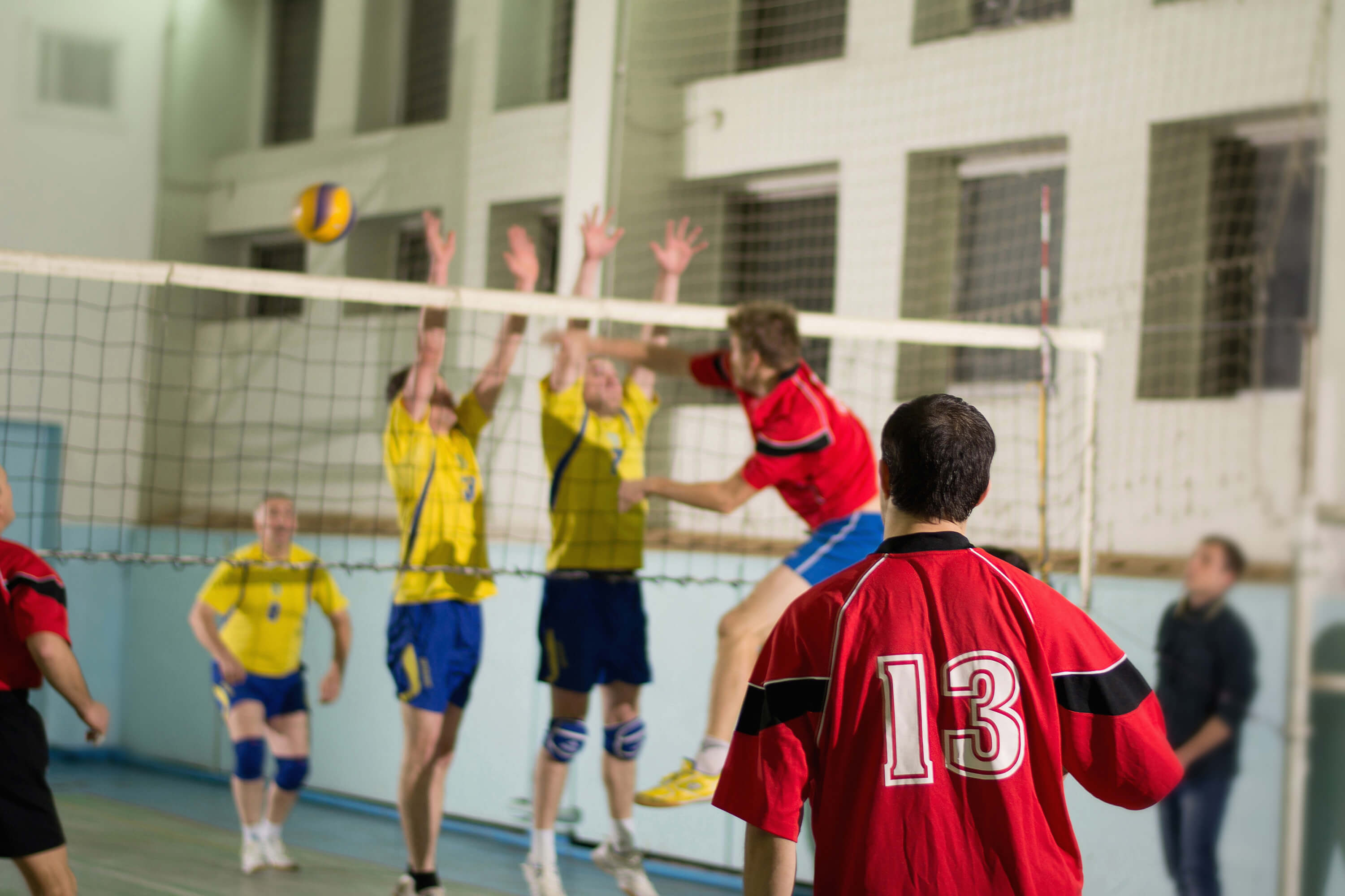 Een volleybalwedstrijd waarbij spelers de smash van de tegenstander proberen te blokkeren